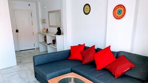 Een moderne woonkamer met een grijze bank, rode kussens, een houten salontafel en een witte deur op de achtergrond.