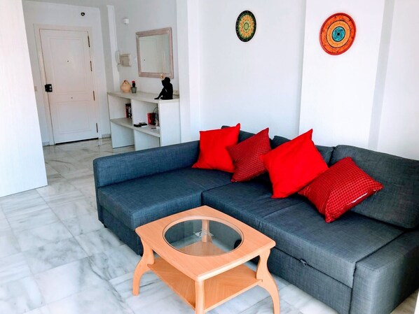 A modern living room with a grey sofa, red cushions, a wooden coffee table, and a white door in the background.