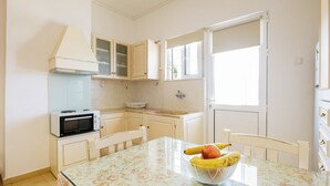 A small kitchen with a microwave, a bowl of fruit on the table, and a window with a view.