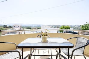 A balcony with a table and chairs, a potted plant, and a view of a cityscape.