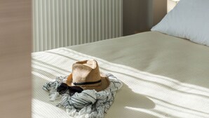 En säng med ett randigt överkast, en hatt, solglasögon och en filt på sig.