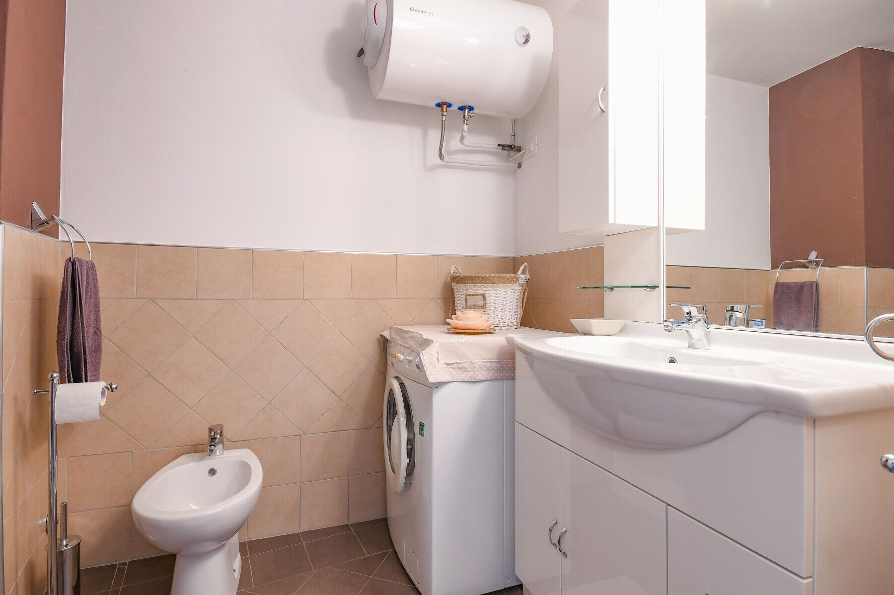 A bathroom with a bidet, a washing machine, a sink, and a mirror.