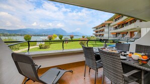 A balcony with wicker chairs and a table set for breakfast, overlooking a lake and mountains. - Sogno del Lago: in front lane of the beach in Manerba del garda (Manerba del Garda)