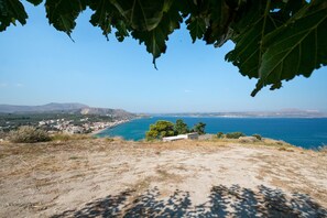 A coastal landscape with a view of the sea, a town in the distance, and a hill with sparse vegetation.