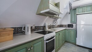 Une cuisine avec des meubles de couleur verte, un réfrigérateur blanc, une cuisinière, un four à micro-ondes et une machine à café.