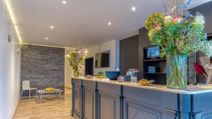 A modern kitchen with a bar area, wooden flooring, and decorative plants. - Hotel Mosa (Oupeye)