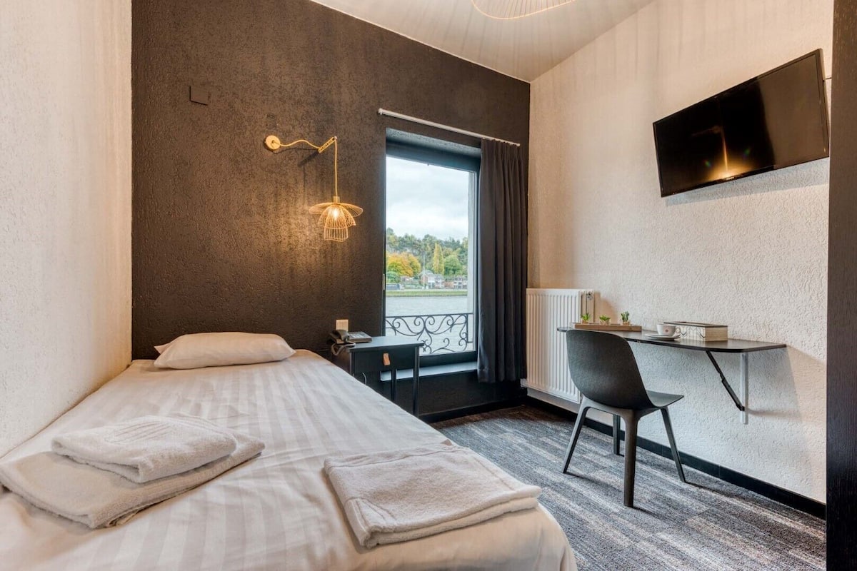 A hotel room with a bed, a desk, a chair, a TV, and a view of the outdoors.