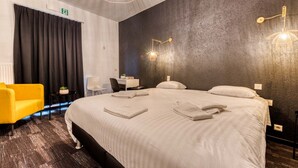 A hotel room with a large bed, a desk, a chair, and a yellow armchair. - Hotel Mosa (Oupeye)