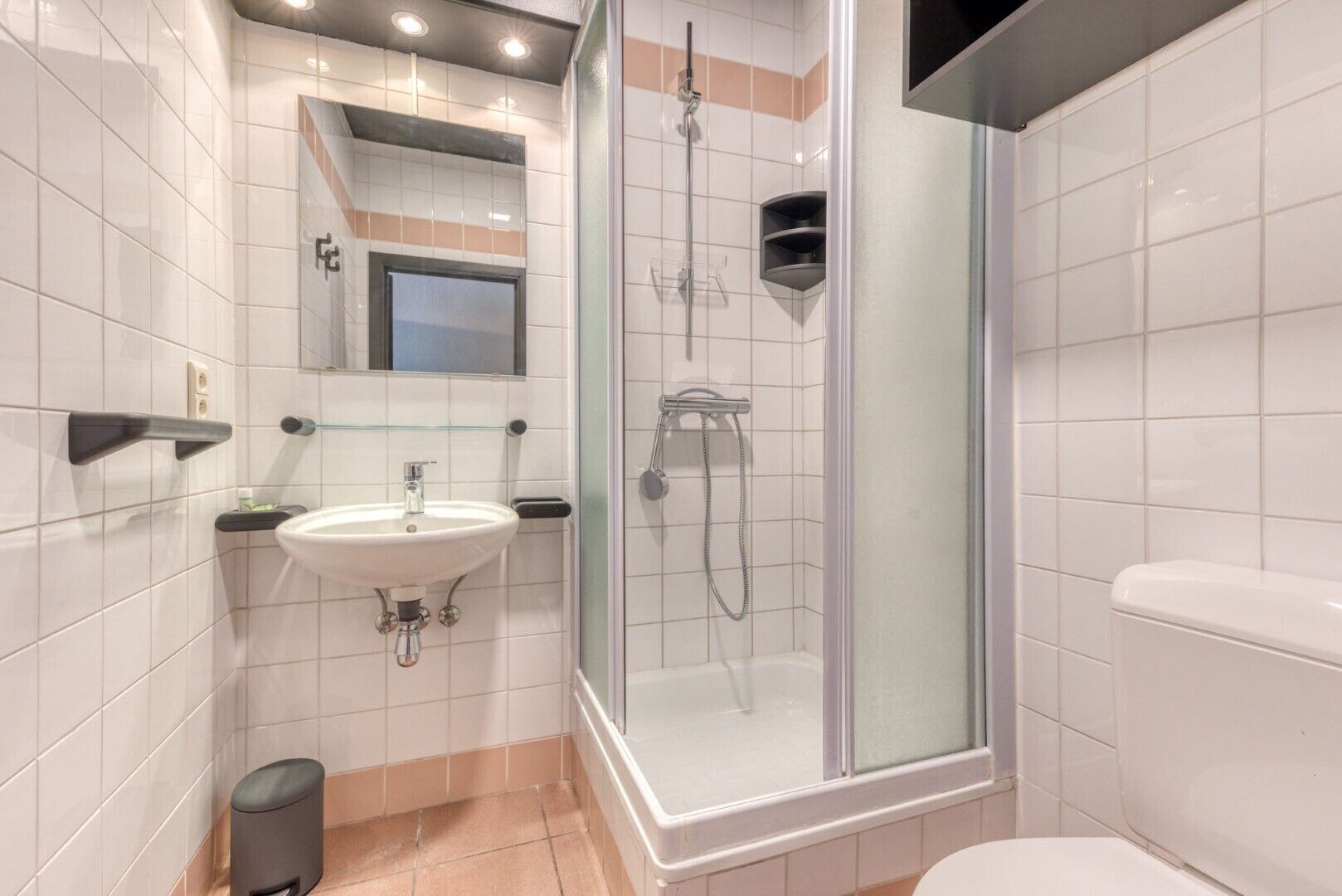 A modern bathroom with a glass-enclosed shower, a white sink, and a toilet.