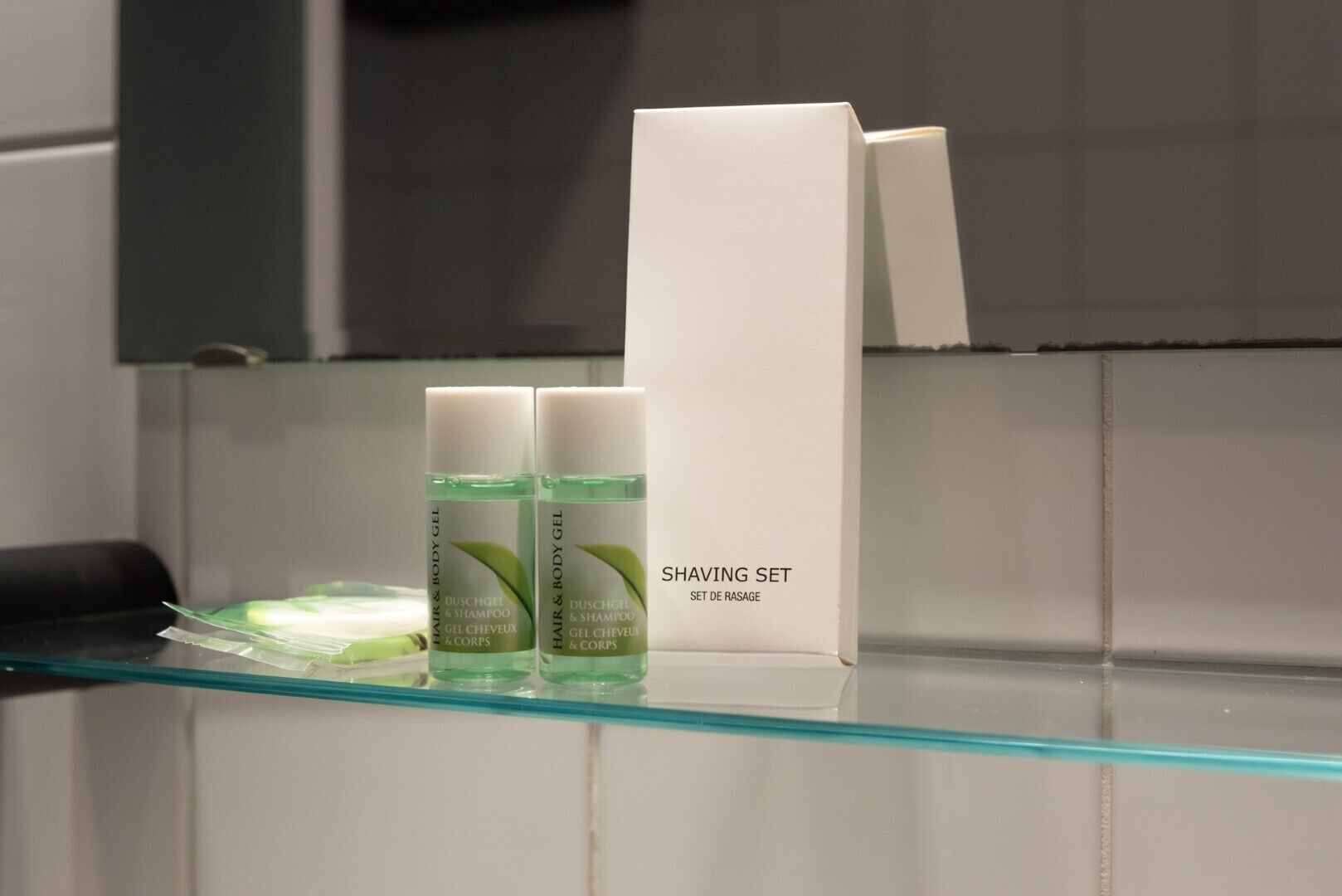 Un baño con un estante de vidrio que contiene un set de afeitado y dos botellas de gel para cabello y cuerpo.