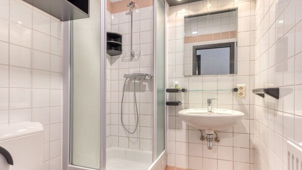 A modern bathroom with a glass-enclosed shower, a white sink, and a mirror above it. - Hotel Mosa (Oupeye)