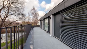 A modern building with a metal balcony, a river, and a tree in the background.