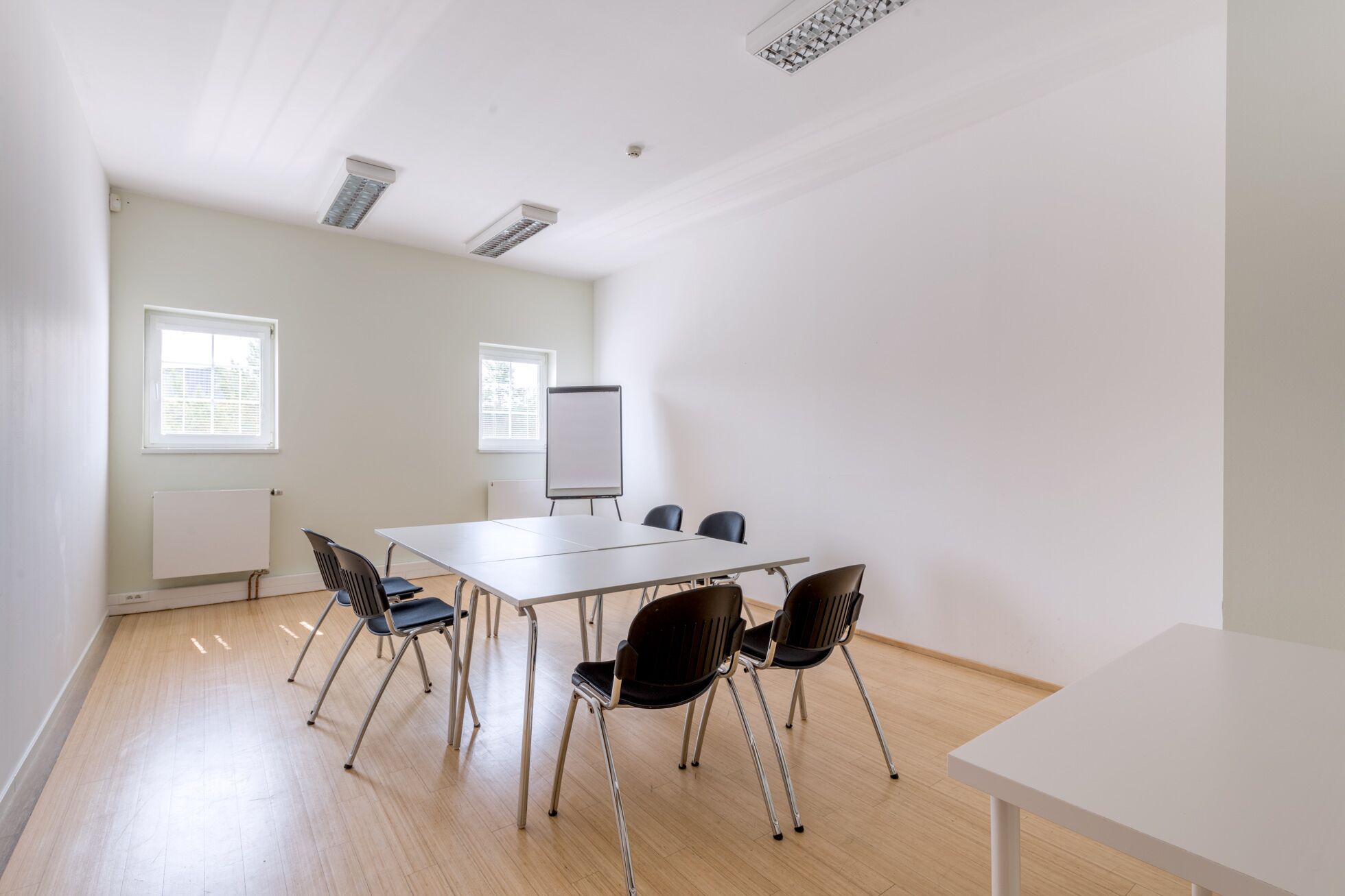 A conference room with a white table, four chairs, a whiteboard, and two windows with blinds.