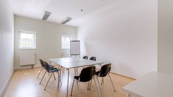 A conference room with a white table, four chairs, a whiteboard, and two windows with blinds.