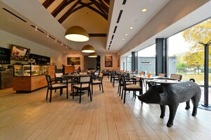 Un restaurante con suelos de madera, mesas, sillas, una estatua de cerdo y ventanas amplias.