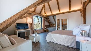 A bedroom with a sloped ceiling, a bed, a desk, a TV, and a window with curtains.