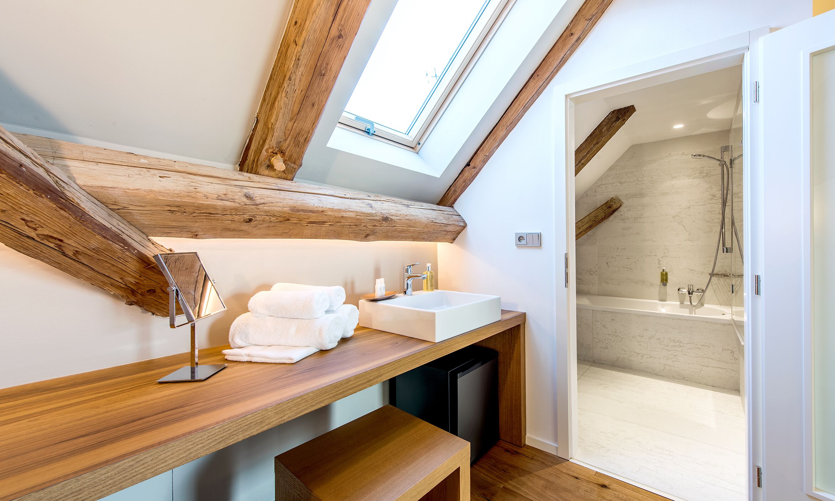 A modern bathroom with a skylight, wooden beams, a sink, and a shower.