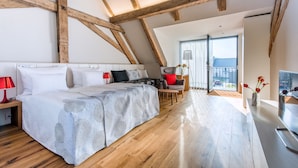 Une chambre moderne avec un grand lit, des poutres en bois, un bureau et une vue sur l’extérieur.