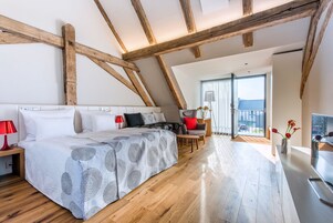 Un dormitorio moderno con una cama grande, vigas de madera, un escritorio y vistas al exterior.