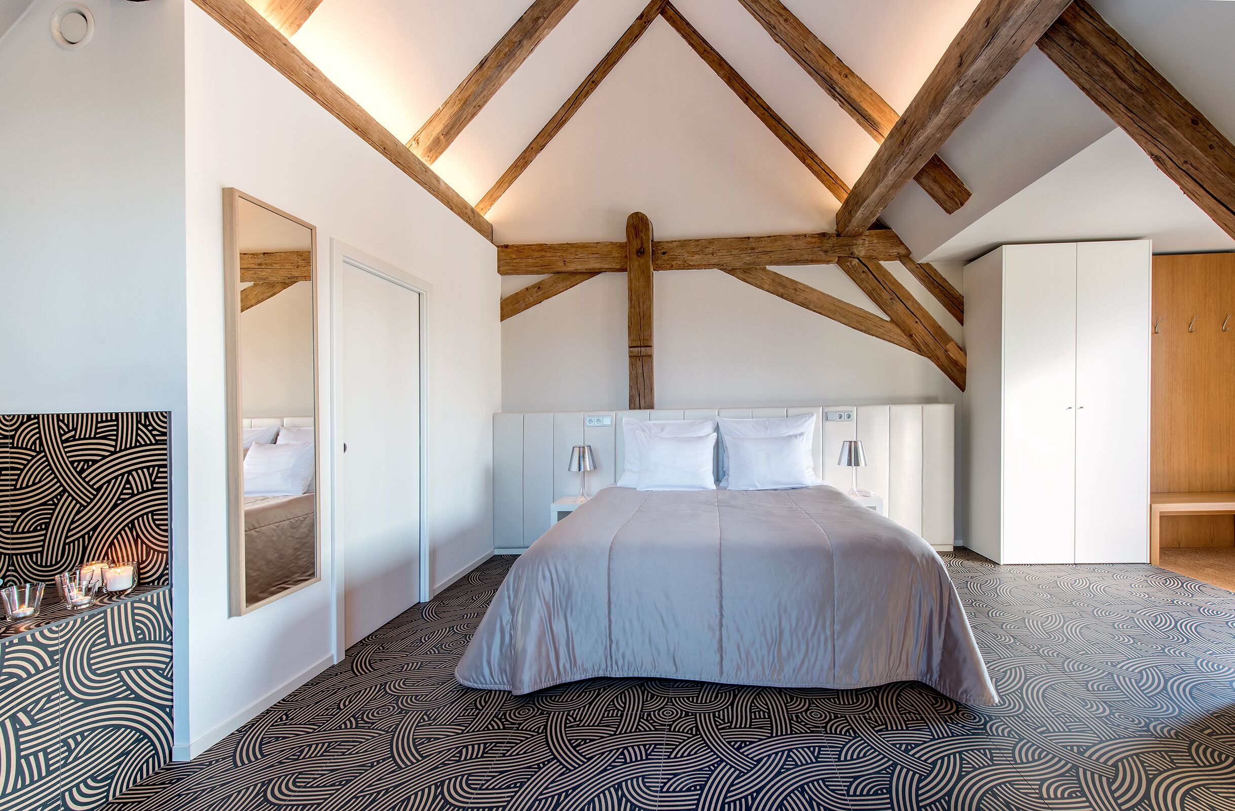 Ein Schlafzimmer mit einem großen Bett, Holzbalken an der Decke, einem weißen Kleiderschrank und einem gemusterten Boden.