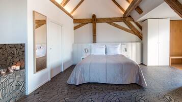 Ein Schlafzimmer mit einem großen Bett, Holzbalken an der Decke, einem weißen Kleiderschrank und einem gemusterten Boden.