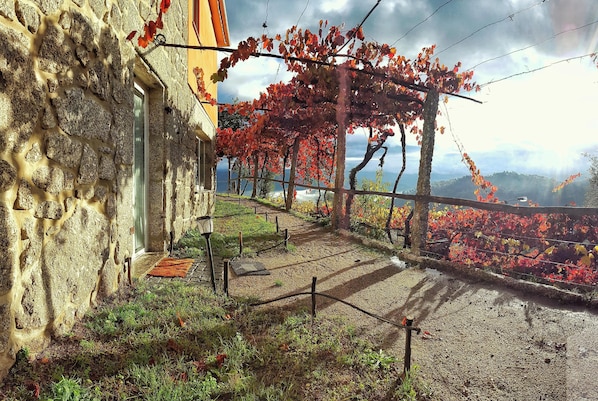 Un bâtiment en pierre avec une porte, un chemin de gravier et une pergola recouverte de plantes grimpantes.