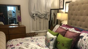 Ein Schlafzimmer mit floralem Bettüberwurf, einem gepolsterten Kopfteil und einem Nachttisch mit Lampe.