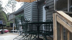 Eine Holzterrasse mit Tisch, Stühlen, einem Sonnenschirm und einer Geländer.