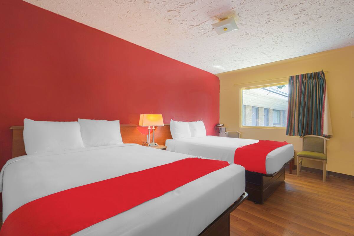Une chambre d’hôtel avec deux lits, une lampe, une chaise et une fenêtre avec des rideaux.