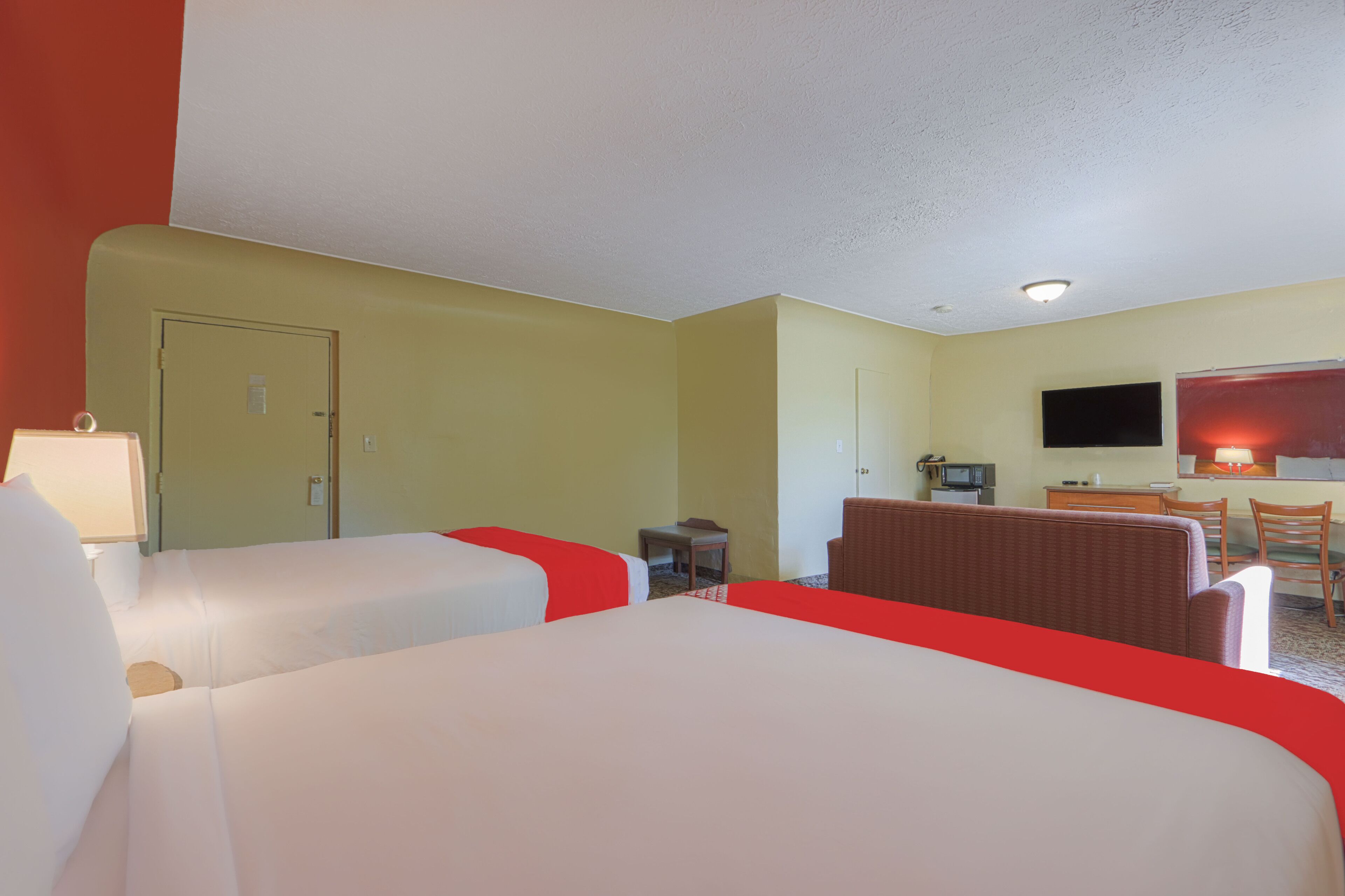 A hotel room with two beds, a desk, a chair, a television, and a microwave.