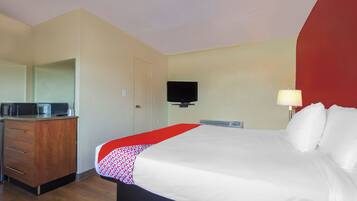 Una habitación de hotel con cama, escritorio con microondas, televisor y una pared de acento roja.