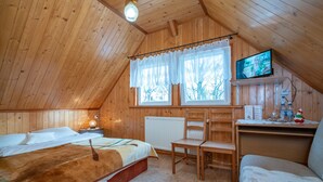 A cozy wooden cabin room with a bed, a chair, a small table, a television, and a window with curtains. - Zającówka (Szklarska Poreba)