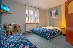 Una camera da letto con due letti, una televisione su uno scaffale, una finestra con tende, un quadro appeso al muro e un comodino con una lampada.