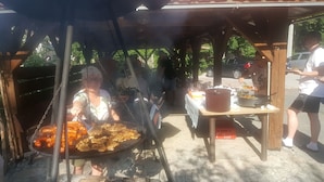 An outdoor barbecue area with a grill, a table with food, and a car in the background. - Zającówka (Szklarska Poreba)