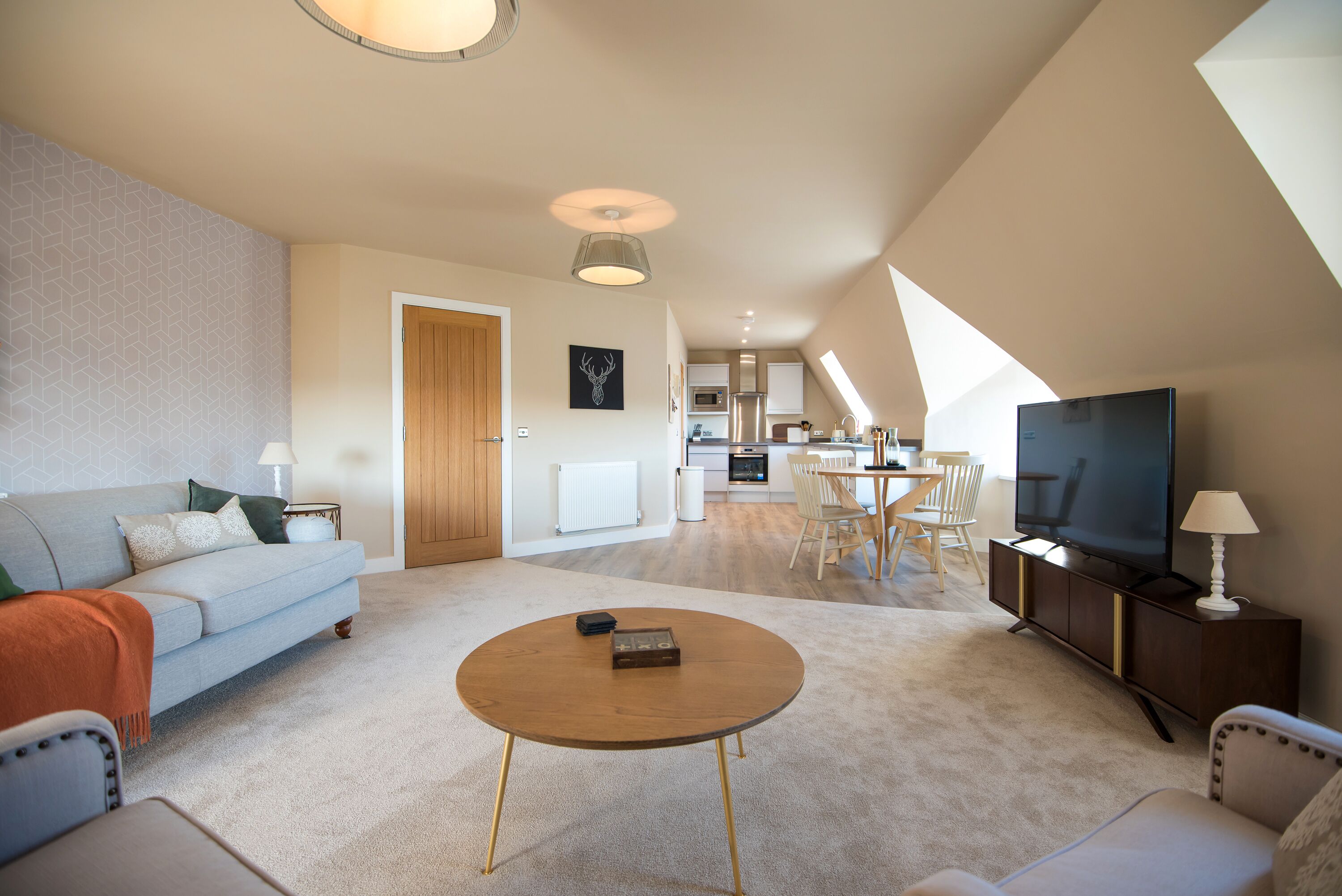 A modern living room with a sofa, coffee table, and TV, connected to a kitchen and dining area.