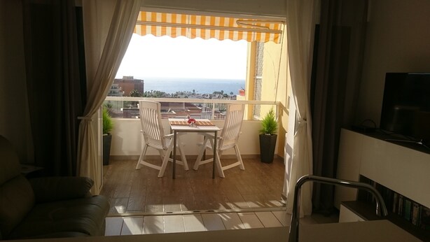 A balcony with a table and chairs, a potted plant, and a view of the sea.