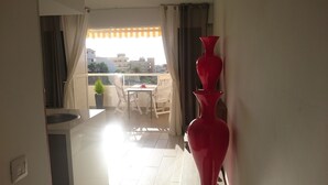 A balcony with a table and chairs, a potted plant, and a red vase.