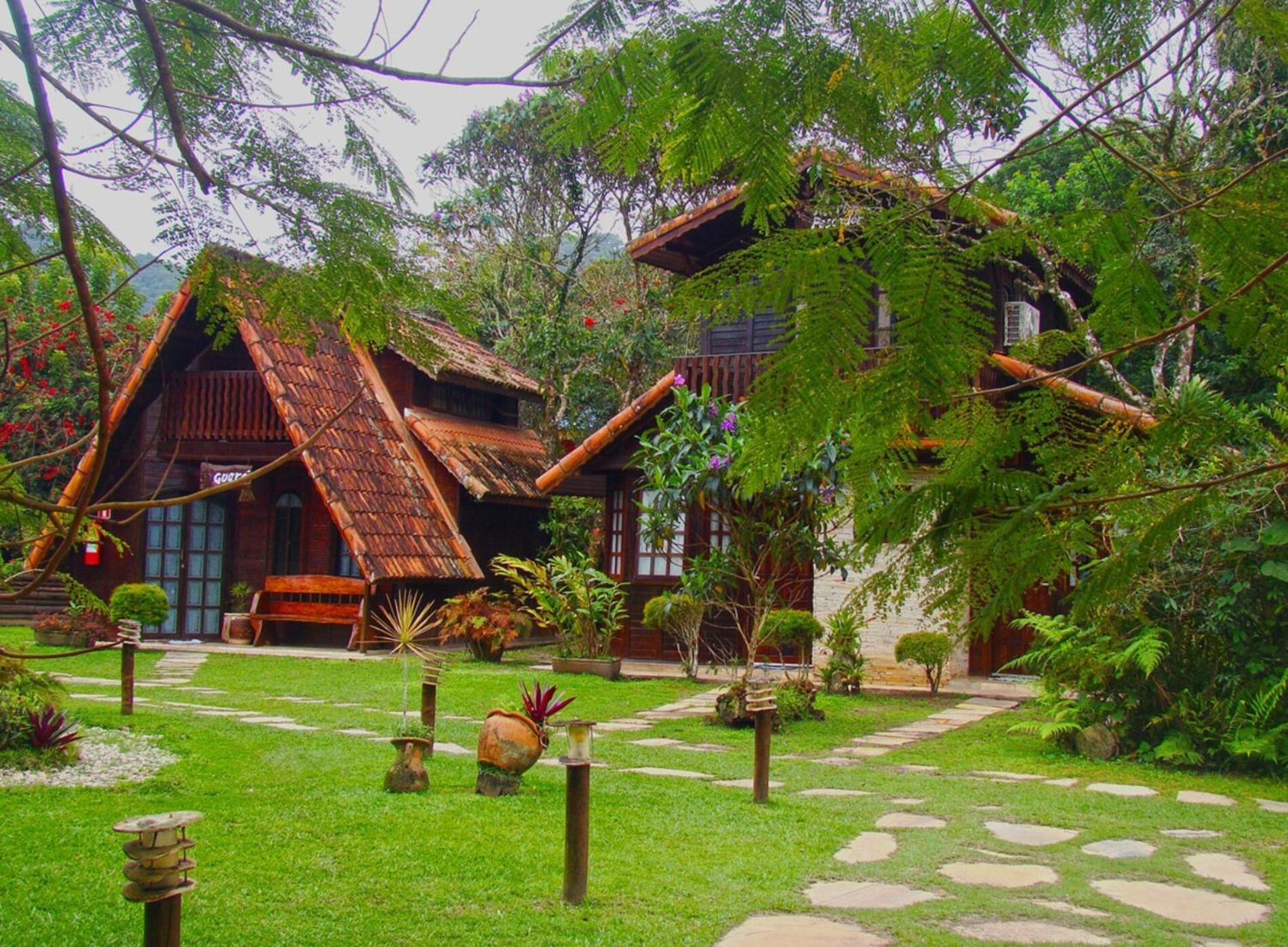 Una casa tradicional con techo de paja y estructura de madera, rodeada de abundante vegetación y un sendero de piedra.