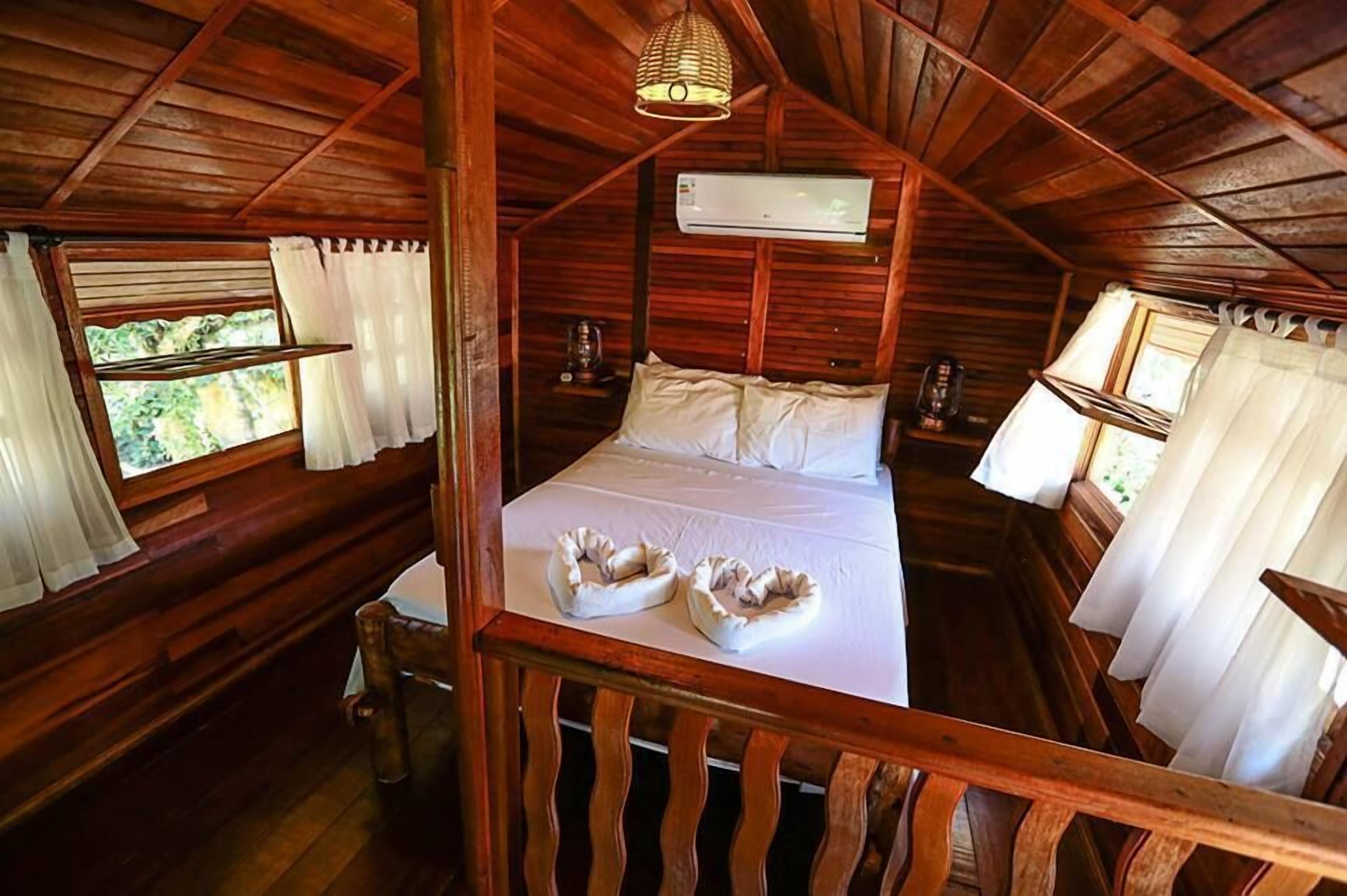 Quarto de cabana de madeira com cama, almofadas e janela.