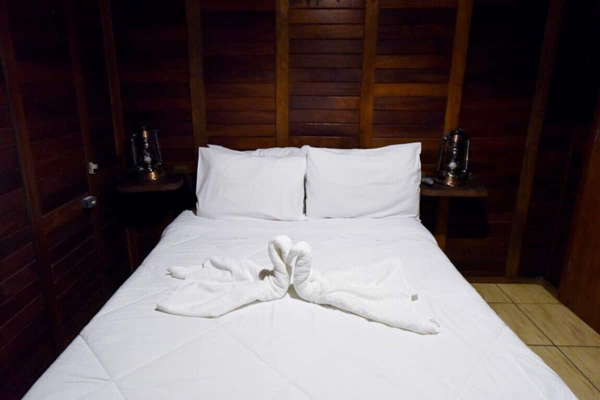 Cama bem arrumada com lençóis brancos e uma toalha dobrada no centro.