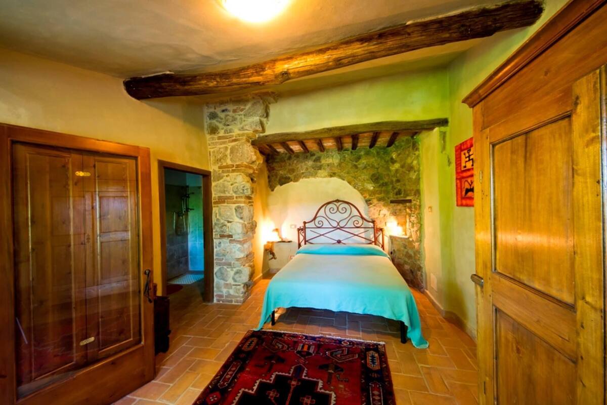 Ein gemütliches Schlafzimmer mit einer Steinwand, einer Holztür, einem Bett mit blauer Bettdecke und einem roten Teppich mit Muster.