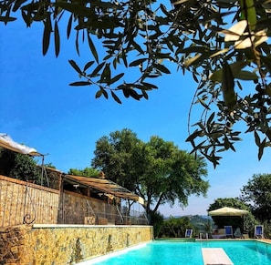 A swimming pool with a stone wall, a wooden deck, and a view of trees and hills. - Agriturismo Piatina (Civitella Paganico)
