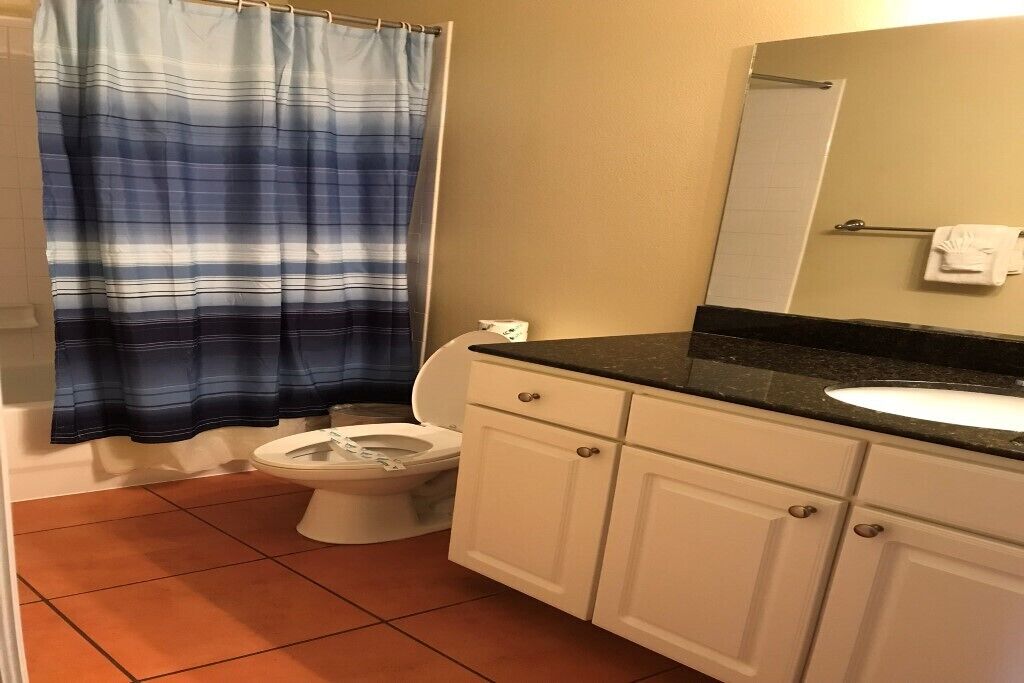 Un baño con inodoro blanco, lavamanos con encimera negra, armarios blancos y cortina de ducha azul a rayas.