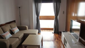 Ein Wohnzimmer mit einer Couch, einem Couchtisch, einem Fernseher und einem Fenster mit Vorhängen.