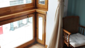 Ein Zimmer mit großem Fenster, Holzboden und einem Korbstuhl.