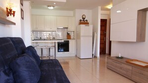 Een moderne woonkamer met een donkerblauwe bank, een keuken met witte kasten, een koelkast en een houten dressoir.
