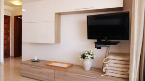 Een moderne woonkamer met een flatscreen televisie aan de muur, een houten salontafel met een bloemenvaas en een stapel kussens.