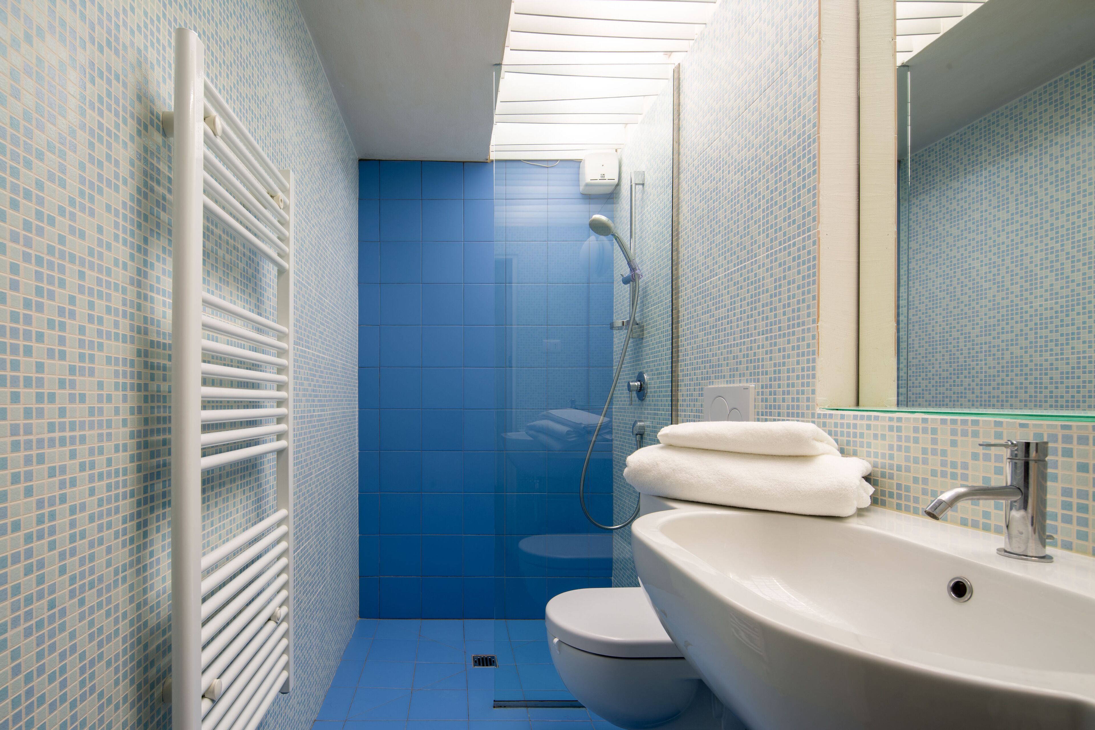A bathroom with a blue tiled wall, a white sink, and a glass shower enclosure.