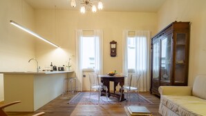 Una sala de estar con sofá, una mesa de comedor con sillas, una zona de cocina con mostrador y pileta, y un gran armario de madera.
