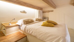 Un dormitorio con cama, mesita de noche, lámpara y una pequeña cómoda.